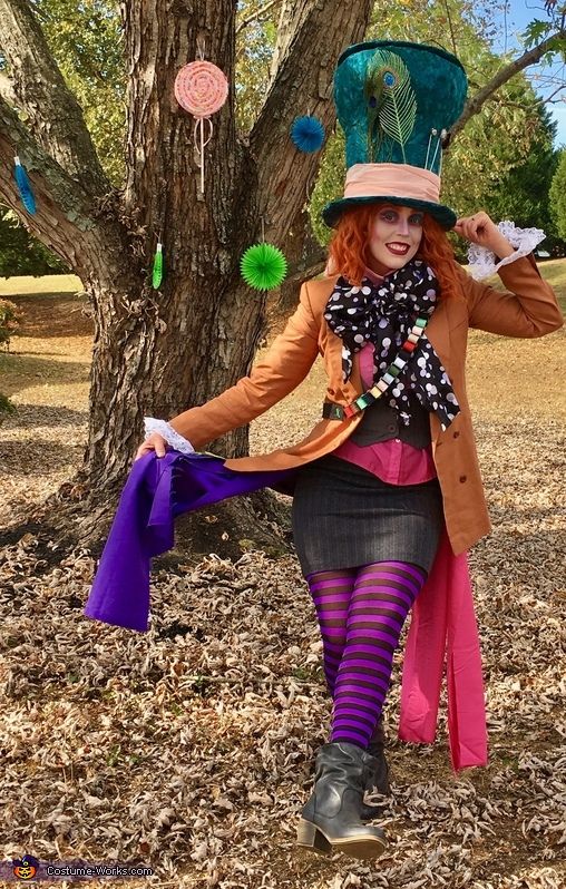 a woman dressed up as a mad hat and holding a purple scarf in front of a tree