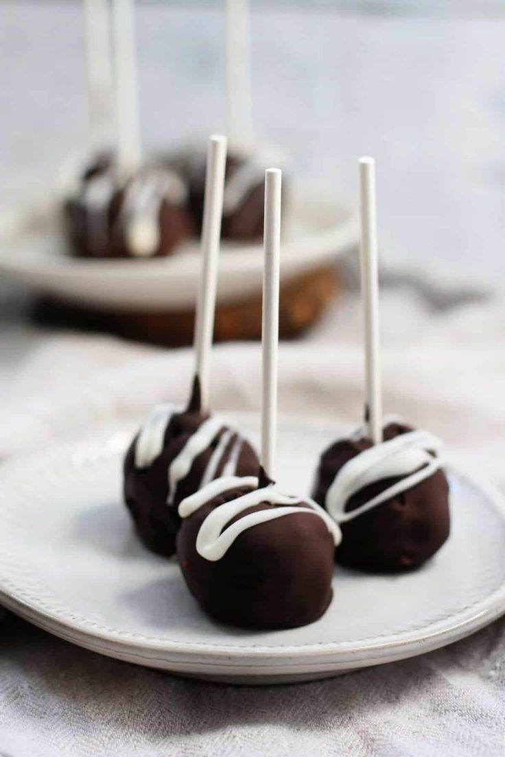 three chocolate covered desserts on a plate with white sticks sticking out of the top