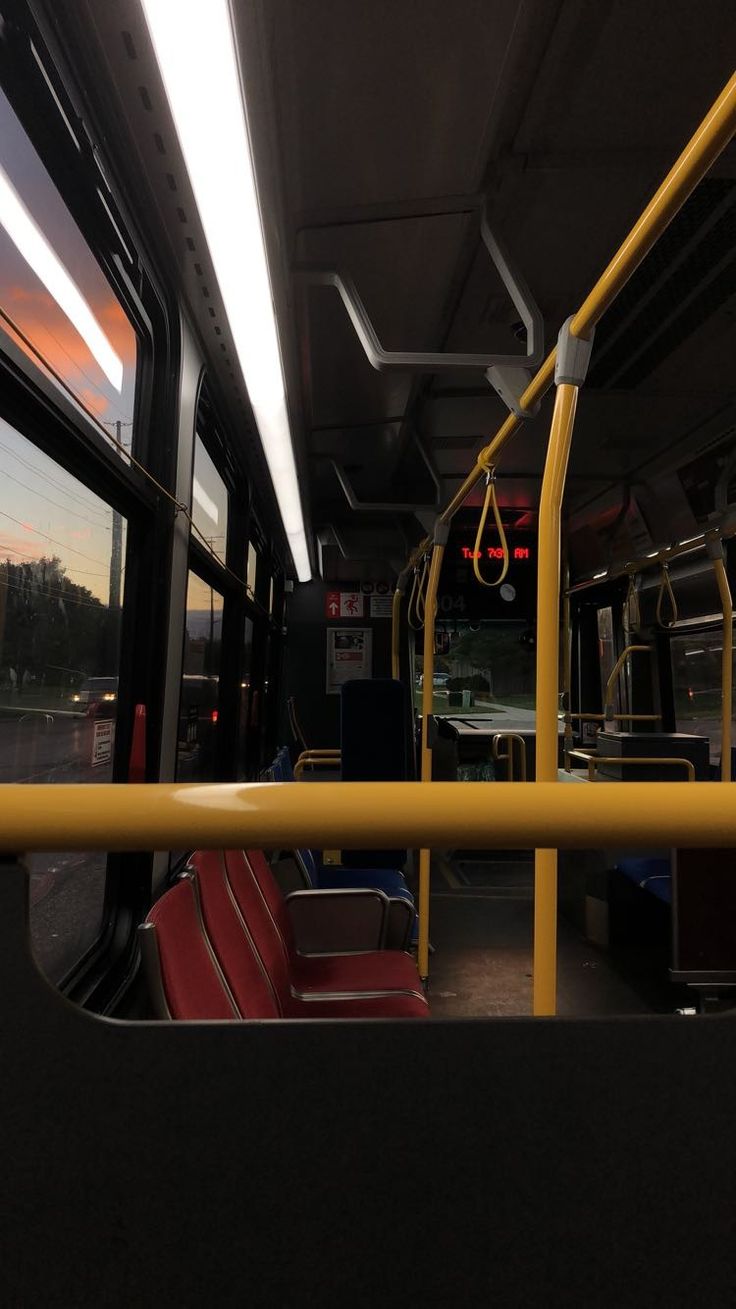 the interior of a bus with red seats and yellow railings at sunset or dawn