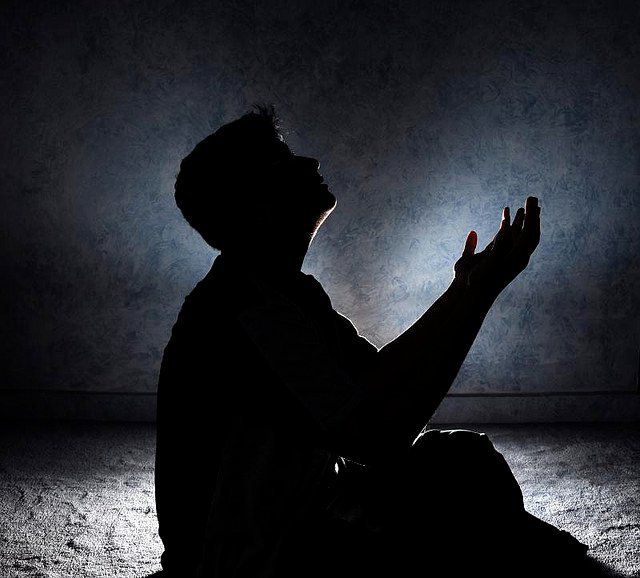 a man sitting in the dark with his hands together