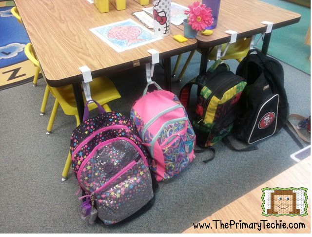 several backpacks are lined up on the floor in front of a table with chairs