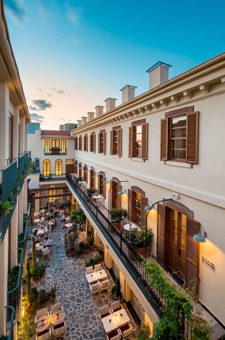 an apartment building with tables and chairs on the balcony at dusk or dawn, overlooking a courtyard