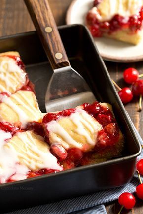 a pan filled with cake covered in icing next to cherries on a table