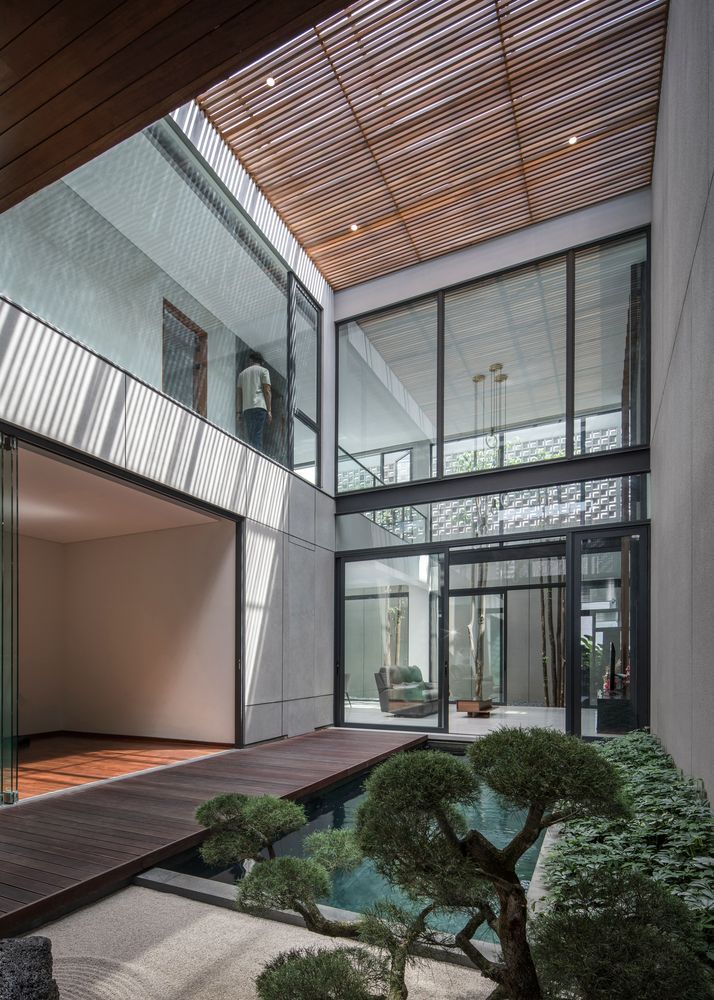 the inside of a house with trees and rocks in front of it, as well as a small pond