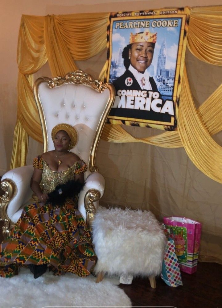 a woman sitting on a white chair in front of a poster and gold drapes