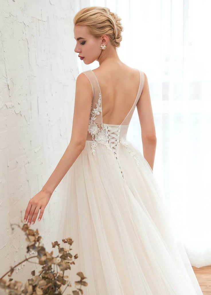 a woman in a white wedding dress standing next to a wall with flowers on it