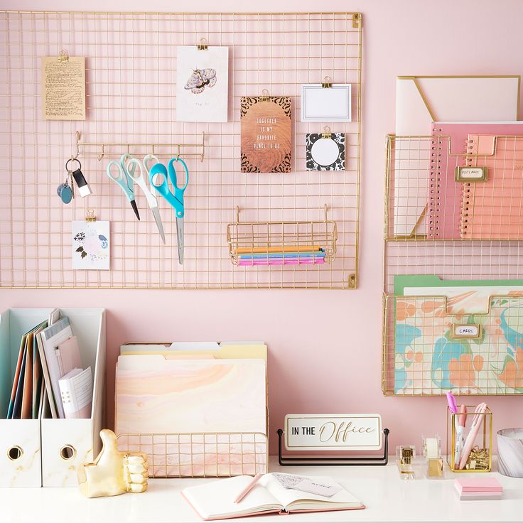 an organized desk with pink walls and lots of office supplies on the wall above it