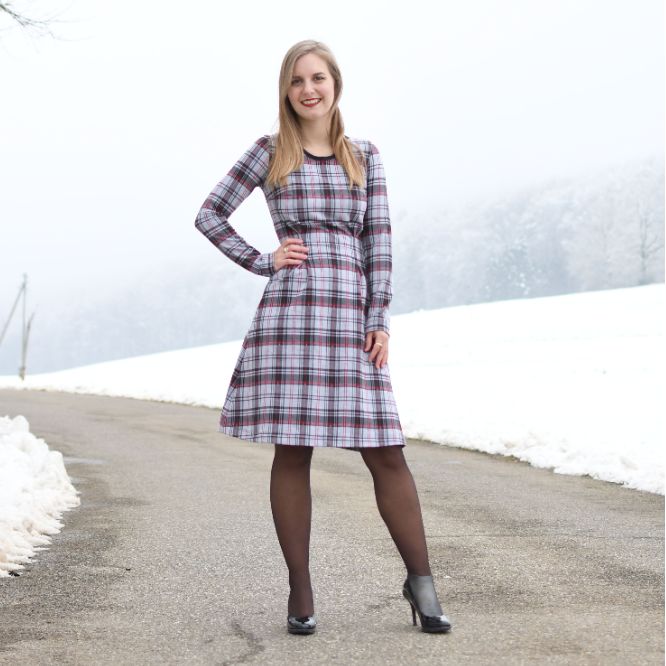 a woman standing in the middle of a road wearing a plaid dress and black tights