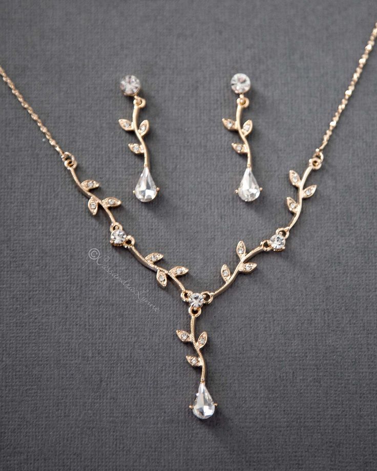 a necklace and earring set with crystal stones on a gray surface, the jewelry is made from gold plated metal