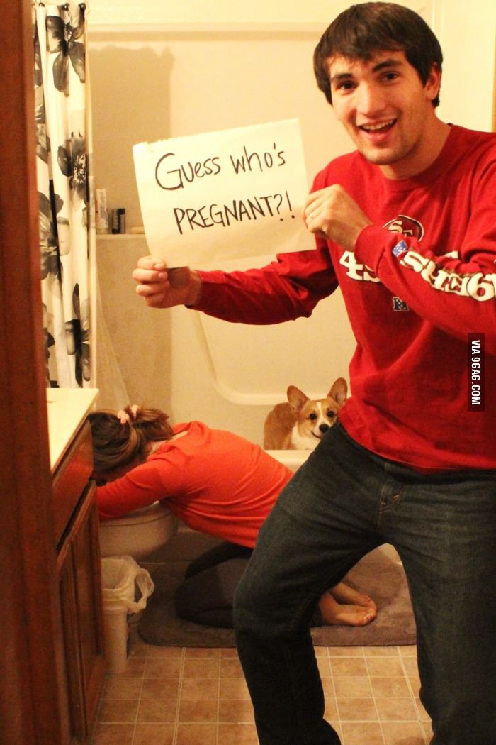 a man holding a sign that says guess who's pregnant? in the bathroom