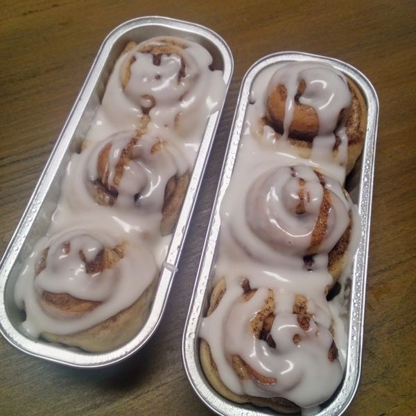 two tins filled with cinnamon rolls covered in icing