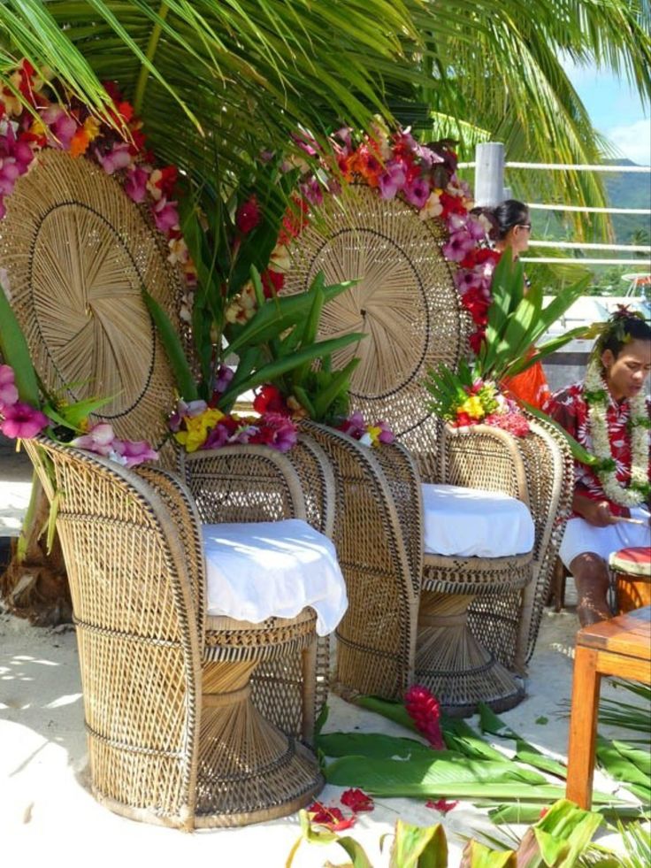 two wicker chairs sitting next to each other in front of a palm tree and flowers