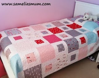 a small bed with a quilt on it in a pink and white room next to a dresser