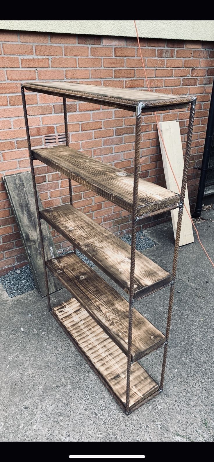 a metal and wood shelf sitting next to a brick wall on the side of a building