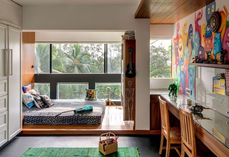 a bedroom with a bed, desk and window in the room that has colorful paintings on the walls