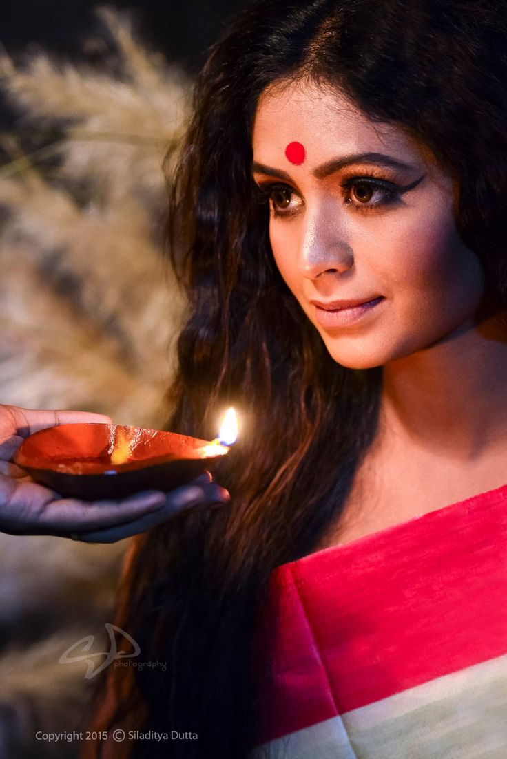 a woman holding a small plate with a lit candle in it's hand while wearing a red and white saree