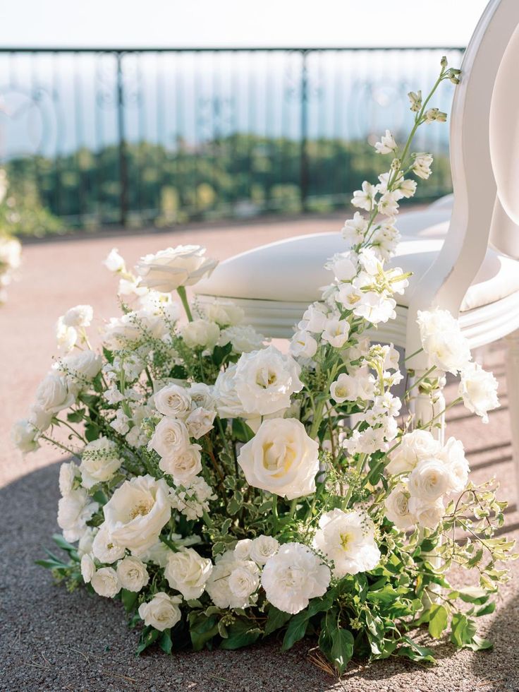 white flowers and greenery on the ground next to a chair