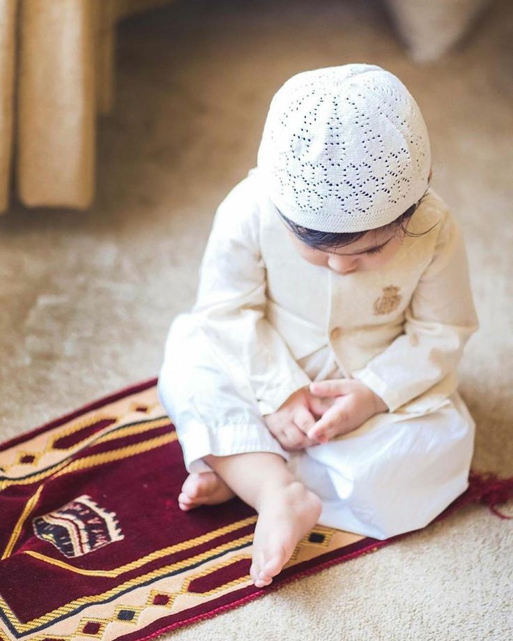 a little boy sitting on the floor playing with his hands while wearing a white outfit