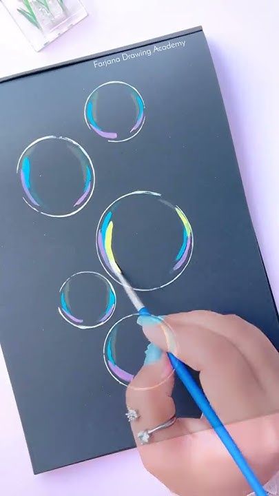 a person is drawing bubbles on a sheet of paper with a blue pencil and watercolors