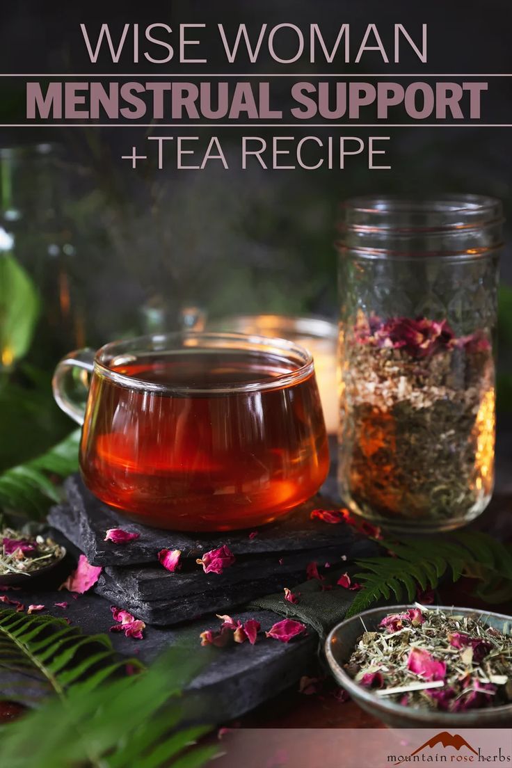 a glass cup filled with tea next to a bowl full of flowers and herbs on top of