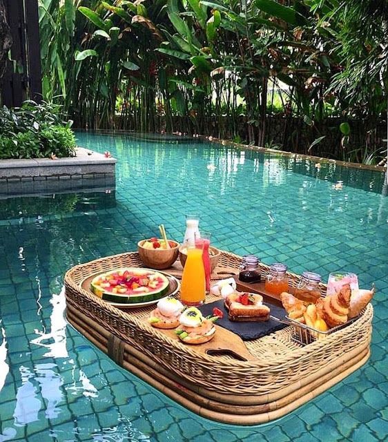 a wicker tray with food on it sitting next to a pool in the middle of a jungle