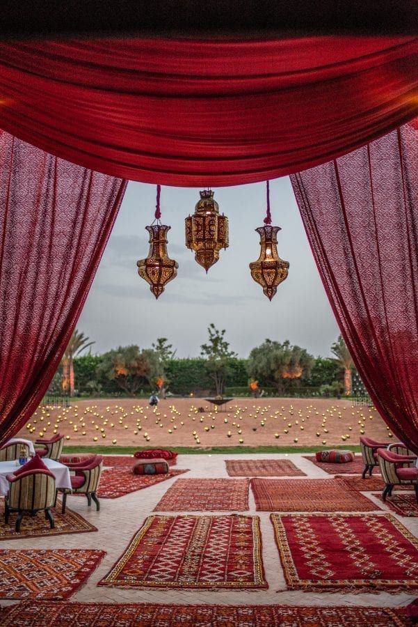 an outdoor dining area with red drapes and chandeliers