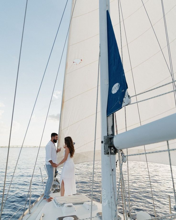 a man and woman standing on the deck of a sailboat