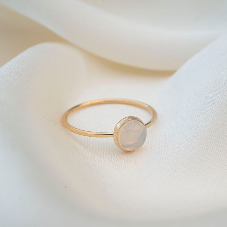 Featuring a stunning 5mm hand picked Australian Opal. Each stone is unique and since these are natural Opals, no two stones will ever be alike. This ring is handmade with a 14k Gold filled ring and a stunning natural opal set in a gold filled bezel. Material: 14k Gold filled Natural Australian Opal Classic Halo Opal Ring For Gift, Minimalist Gold Opal Rings, Opal Ring With Bezel Setting, Gold Round Cut Opal Ring, Delicate 14k Gold Opal Ring Gift, Minimalist Gold Opal Birthstone Ring, Minimalist Adjustable Opal Ring For Anniversary, White Minimalist Opal Ring Birthstone, Classic Opal Round Rings