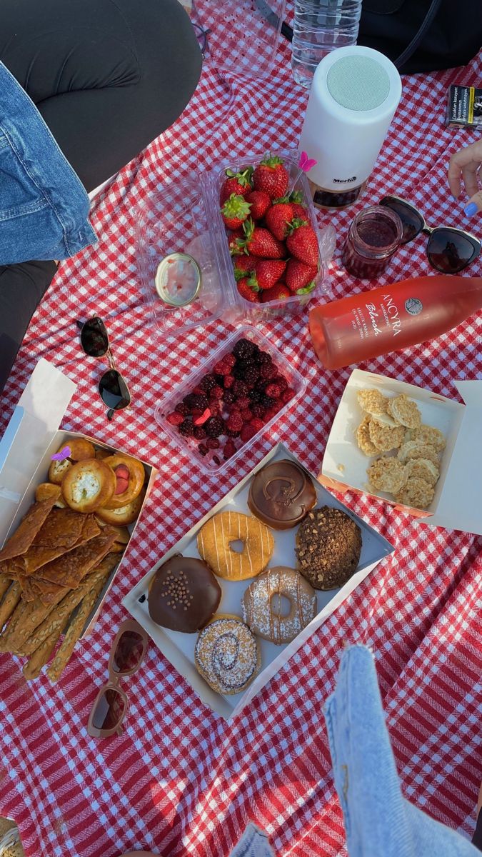 a picnic table topped with donuts, strawberries and other snacks on top of a red and white checkered cloth