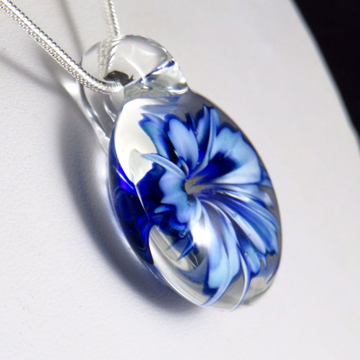 This unusual and unique pendant has a realistic blue and white glass 3D flower inside a solid glass - this isn't resin or a real flower, it's all made entirely of glass! I've used a cobalt blue over white, which I've graduated in tone and to form bands on the petals to make the flower look more realistic, also giving the edges and centre a darker rim of blue. In the centre I've added some yellow 'stamens' to make it look more realistic, where some bubbles have clustered around them to add a dew White Glass Round Pendant Necklace, Silver Glass Flower Pendant Jewelry, Blue Flower Pendant Jewelry Gift, Glass Jewelry With Large Pendant As A Gift, Blue Flower Pendant Jewelry As Gift, Flower Shaped Glass Necklace For Gift, White Flower Shaped Glass Jewelry, Elegant Glass Flower Necklace, Elegant Glass Flower Necklaces