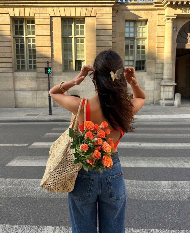 a woman is standing on the street with her back to the camera and holding a bouquet of flowers