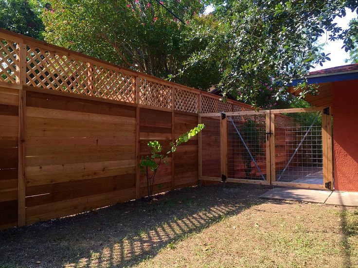 a wooden fence next to a red building and tree in the yard with grass on the ground