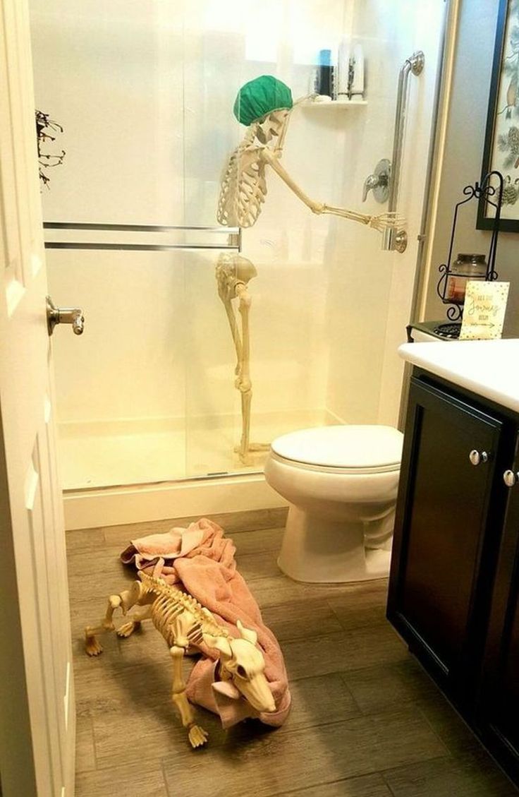 a bathroom with a skeleton on the floor and a toilet in the shower stall behind it