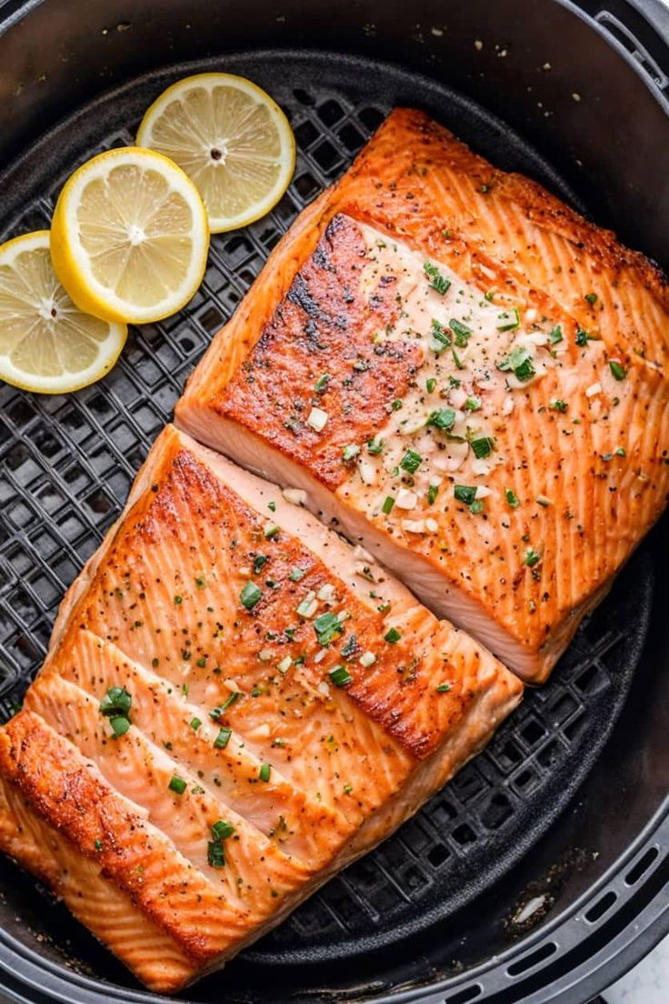 two salmon fillets in an air fryer with lemons and parsley on the side