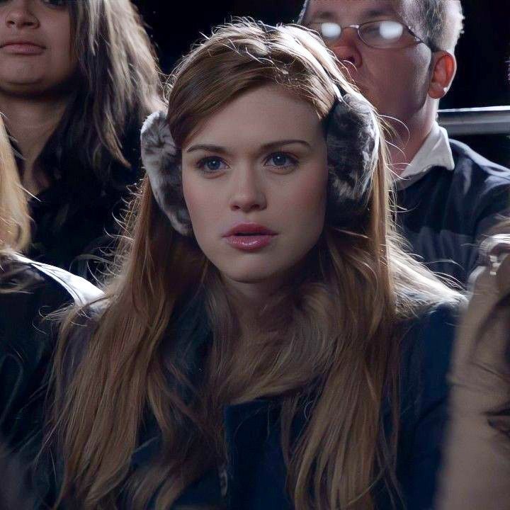 a woman with long hair wearing ear muffs sitting next to other people in the audience