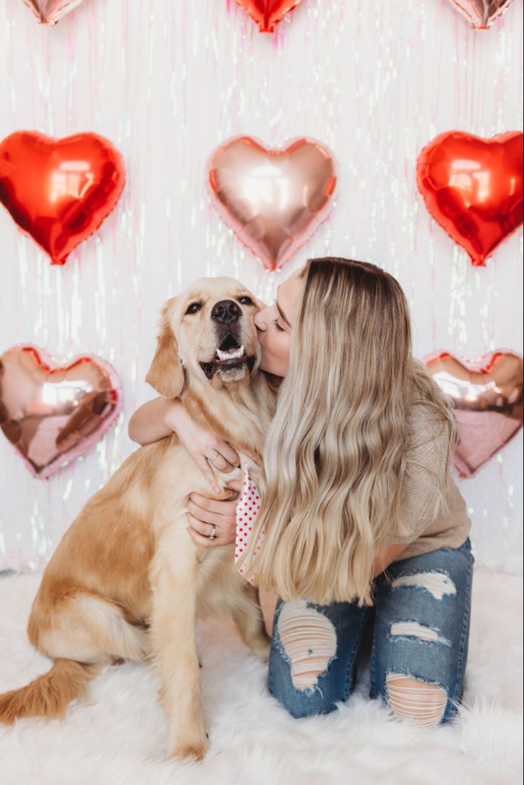 a woman kissing her dog in front of heart shaped balloons