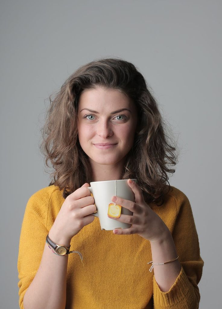 a woman is holding a cup and looking at the camera while wearing a yellow sweater