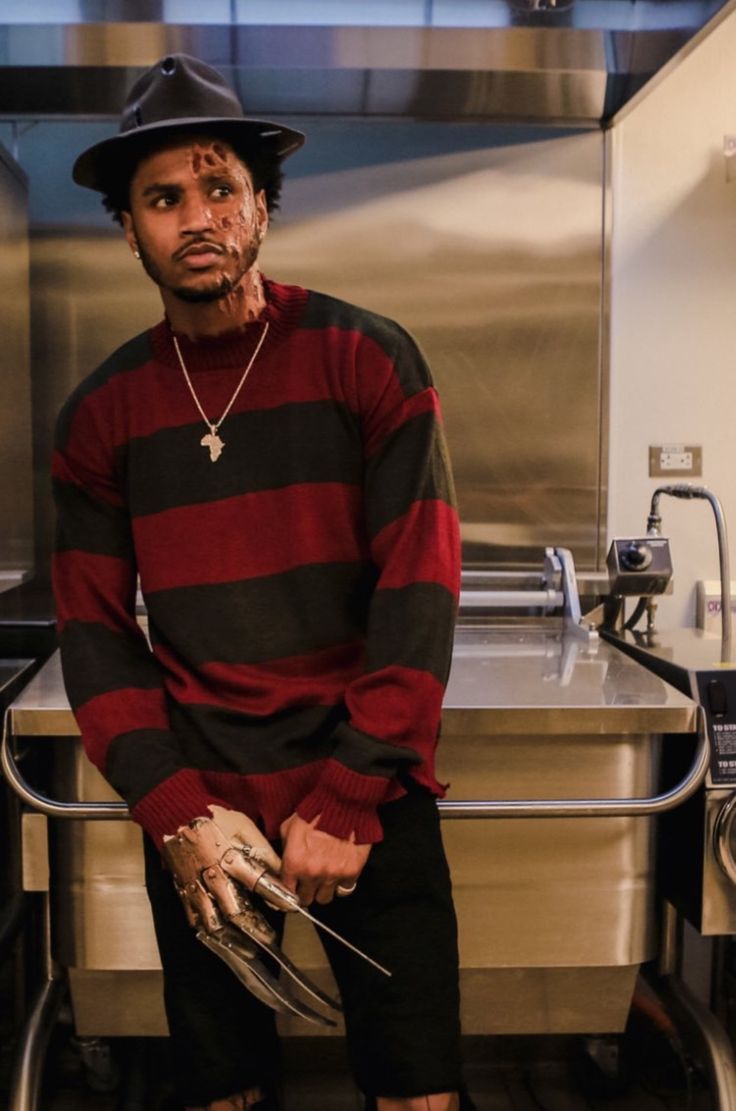 a man in a black hat and red striped shirt standing next to a kitchen sink