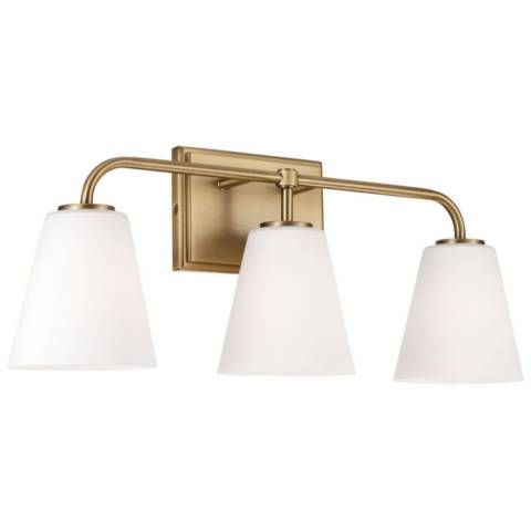 three light bathroom fixture with white glass shades on an antique brass finish wall mounted lamp