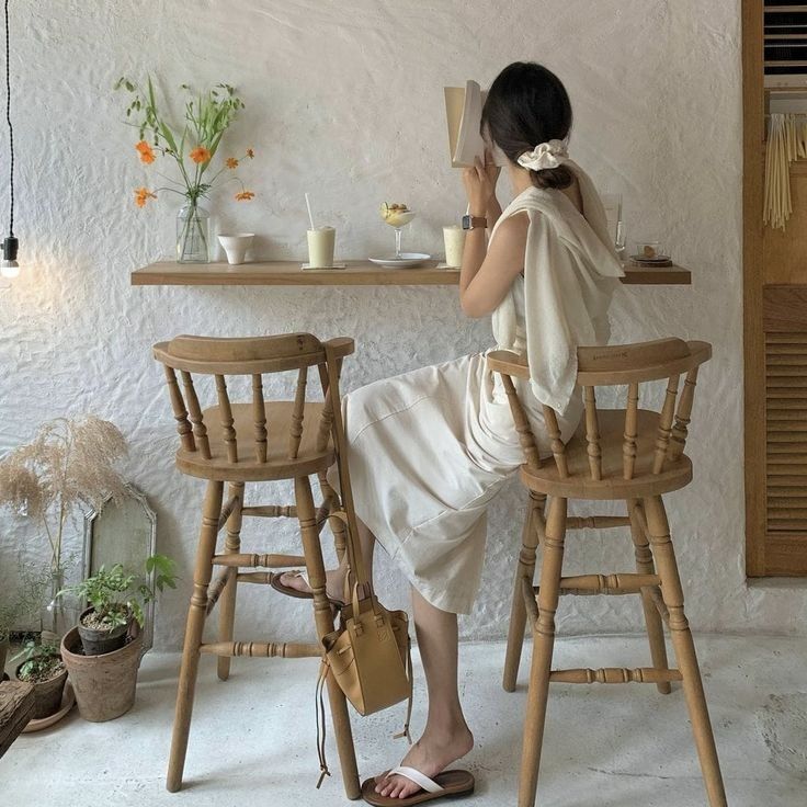 a woman sitting at a table in front of two wooden chairs with cups on them