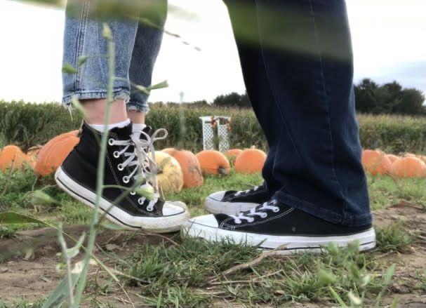 two people standing next to each other in front of pumpkins on the ground and grass