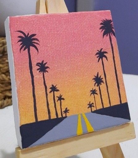 an easel with a painting on it that has palm trees painted on the side