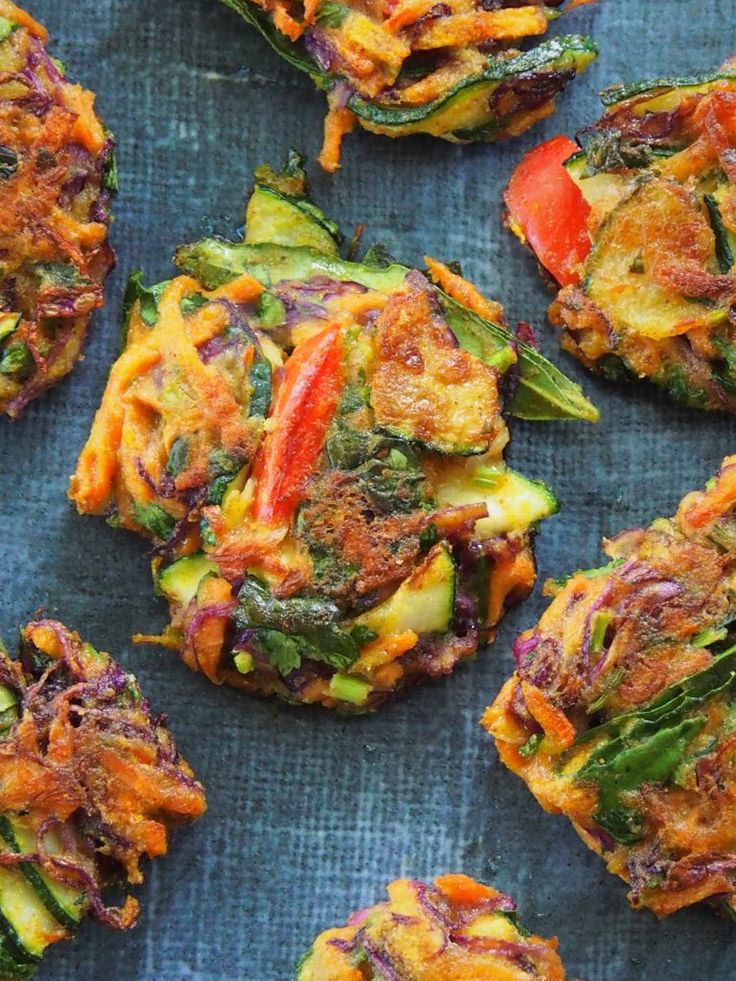 several different types of food are on a blue tablecloth and one is topped with broccoli, red peppers, and other vegetables