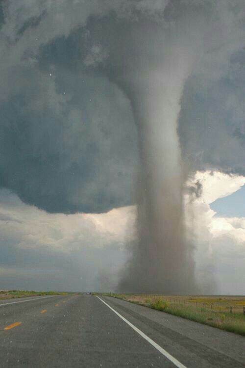 a large tornado is coming out of the sky over an empty road on a cloudy day