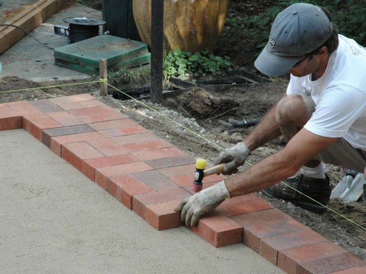 a man laying bricks on top of a sidewalk