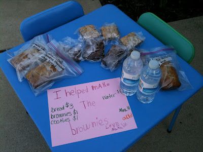 a blue table topped with lots of bags of food and water next to a sign