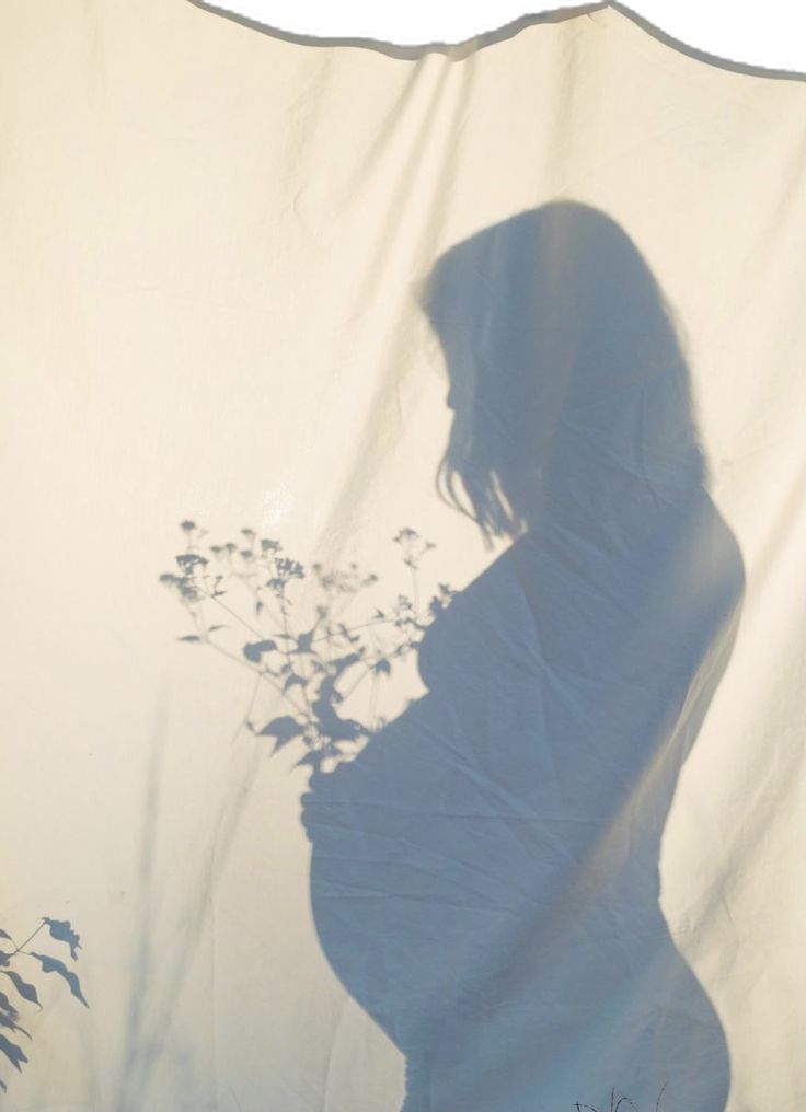 a pregnant woman standing in front of a white curtain with flowers on it's side