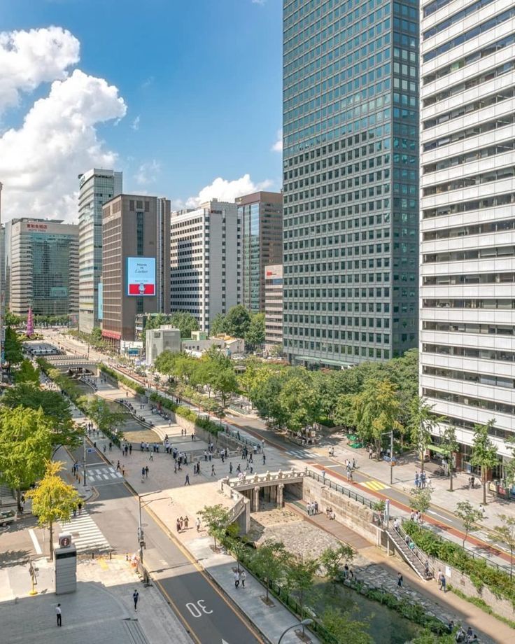 This is a photo of a city street with tall buildings. The image includes tags such as outdoor, cloud, tower block, metropolitan area, commercial building, tree, building, urban area, sky, metropolis, downtown, mixed-use, condominium, urban design, cityscape, skyline, daytime, skyscraper, road, apartment, corporate headquarters, street, tower, and city. Japan Tokyo Wallpaper, Cheonggyecheon Stream, Tokyo Wallpaper, Korea Store, Welcome To Korea, Seoul Korea Travel, Cool City, Beautiful Blue Sky, South Korea Seoul