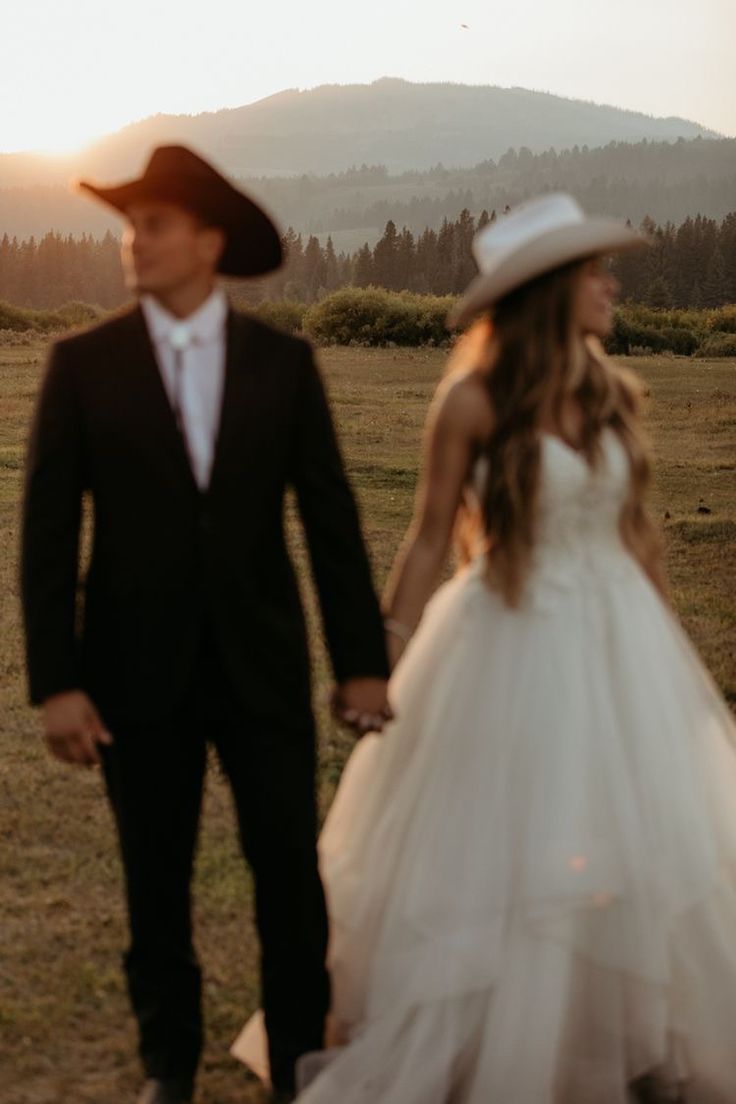 a bride and groom are walking in the field at sunset with mountains in the background