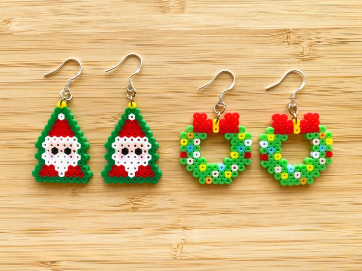 three christmas themed beaded earrings on a wooden surface, one with a santa clause and the other with a snowman